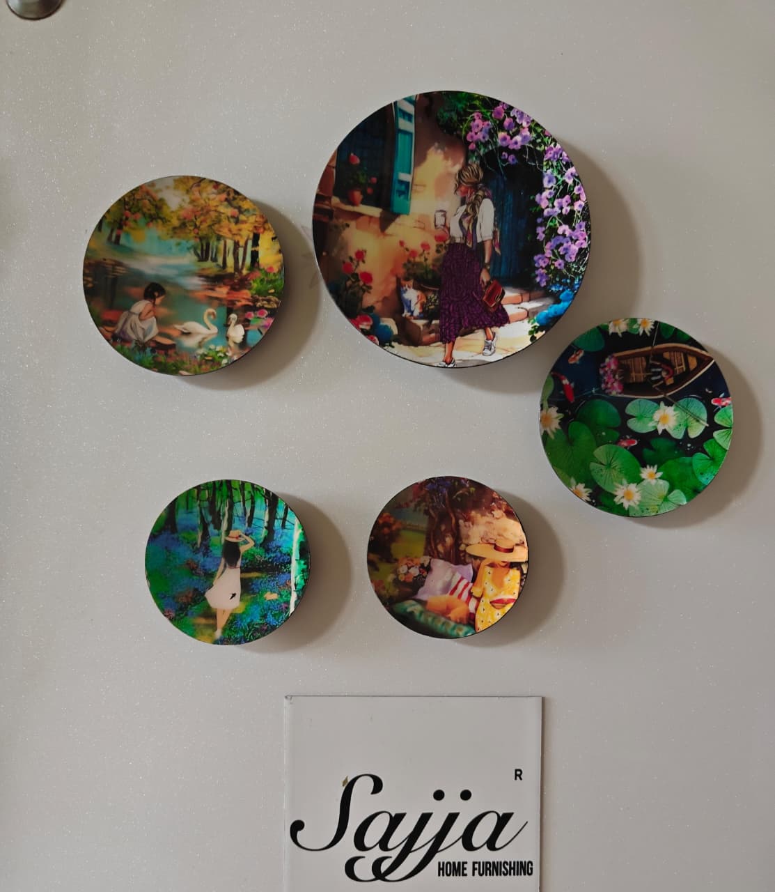 Five decorative plates with artistic designs on a wall, featuring the brand 'Sajja Home Furnishing'.