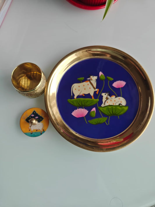 Decorative plate with cow and lotus design on a blue background, placed on a white surface.