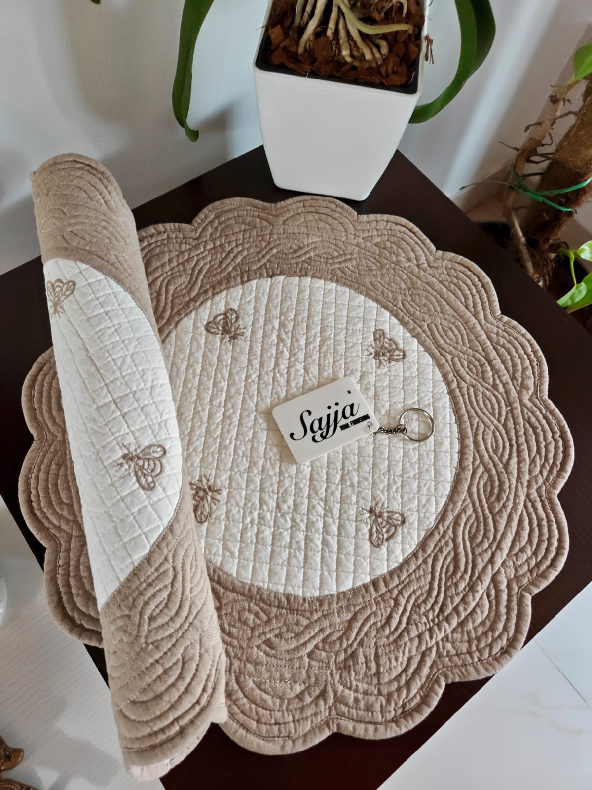 Round quilted placemat with decorative border on a table, featuring the brand 'Sujia'.